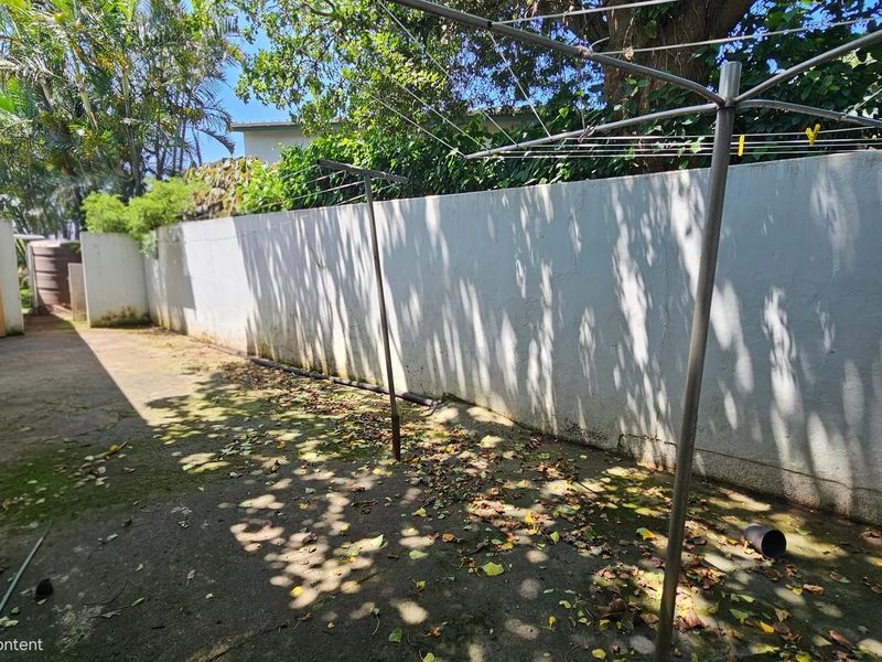 A rear exterior area featuring concrete paving, a boundary wall, and a rotary clothesline, requiring maintenance and landscaping to improve its overall appeal.