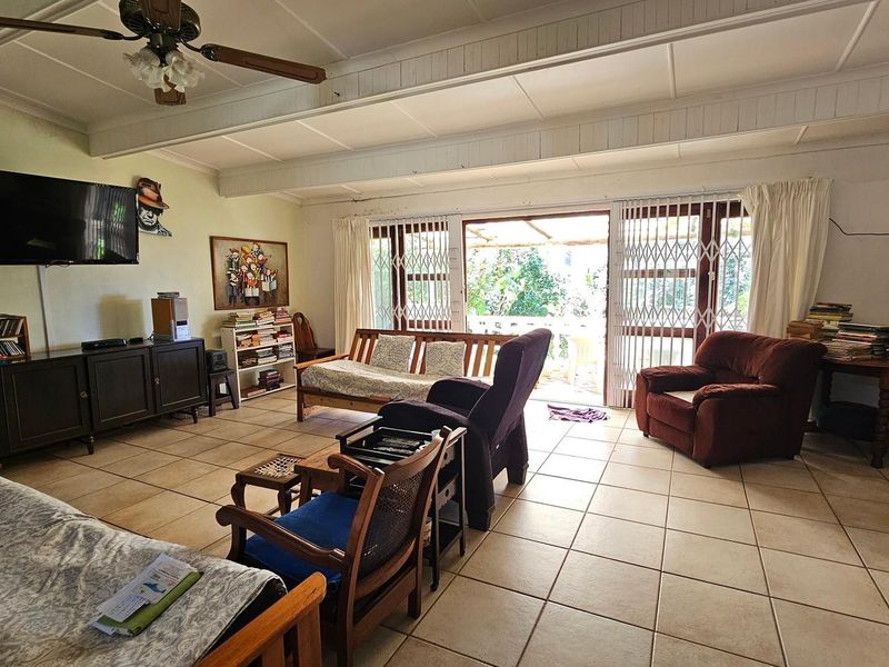 Spacious living room featuring ceramic tiled flooring, exposed beam ceilings, a ceiling fan, and sliding glass doors providing access to the outdoor patio area.