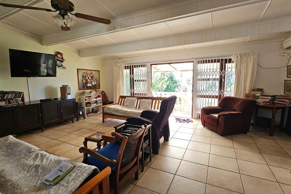 Spacious living room featuring ceramic tiled flooring, exposed beam ceilings, a ceiling fan, and sliding glass doors providing access to the outdoor patio area.