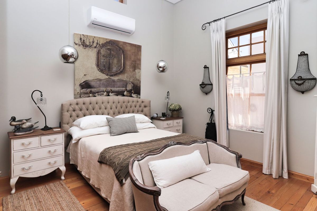 A well-maintained bedroom featuring polished timber flooring, a split-system air conditioning unit, and classic window joinery.