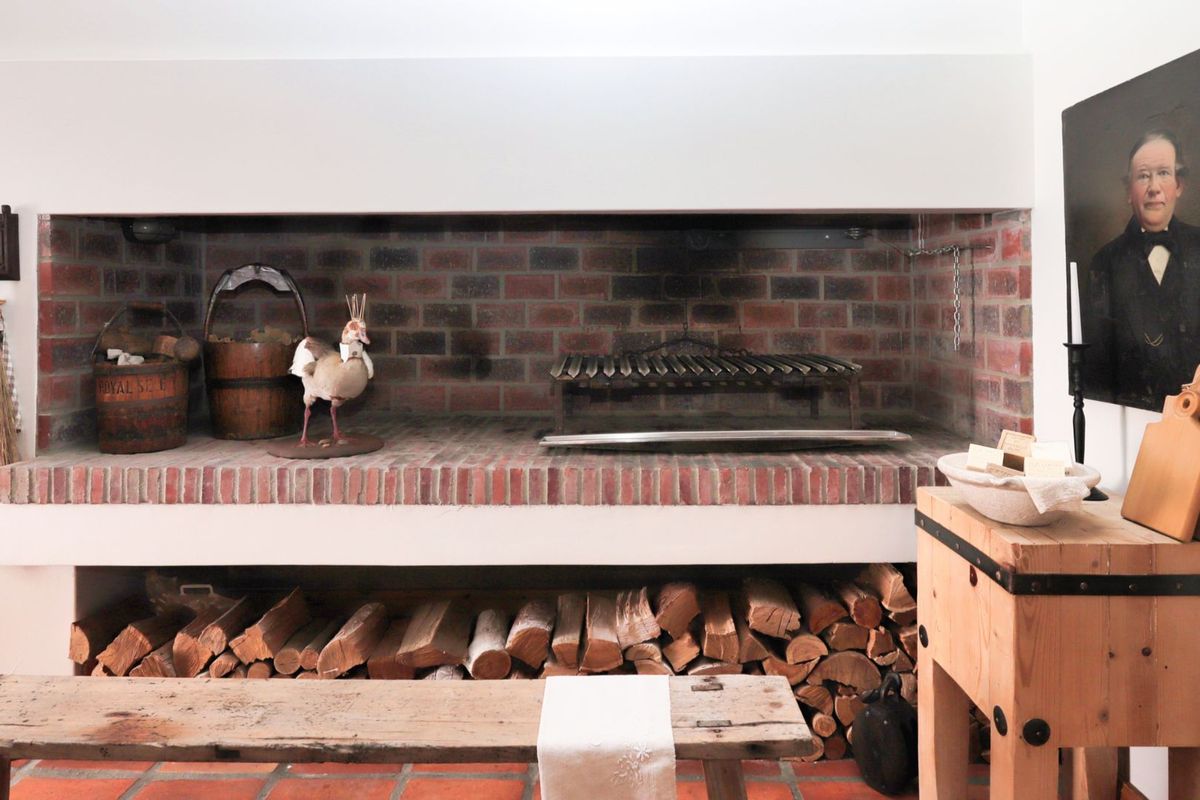 A rustic indoor fireplace featuring exposed brickwork, a built-in hearth, and integrated firewood storage, creating a warm and traditional atmosphere.