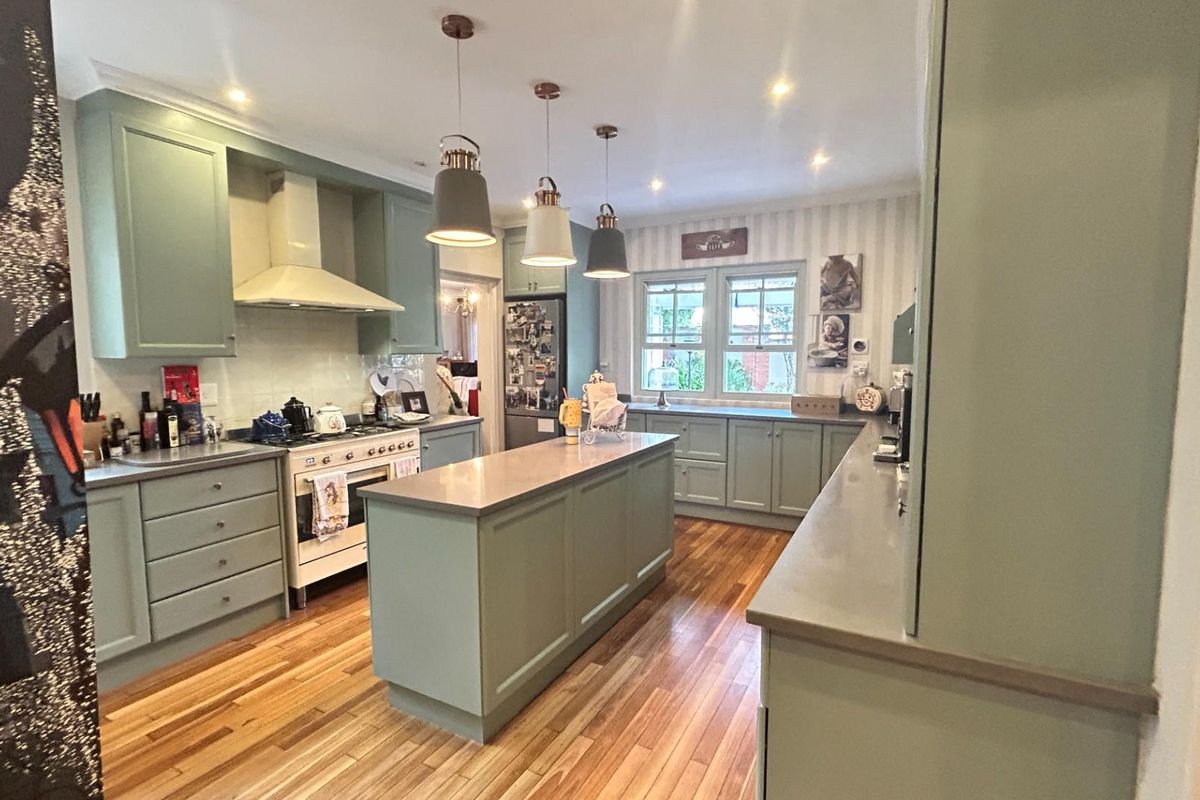 A well-appointed kitchen featuring sage green cabinetry, a central island, stone countertops, hardwood flooring, and integrated stainless steel appliances.