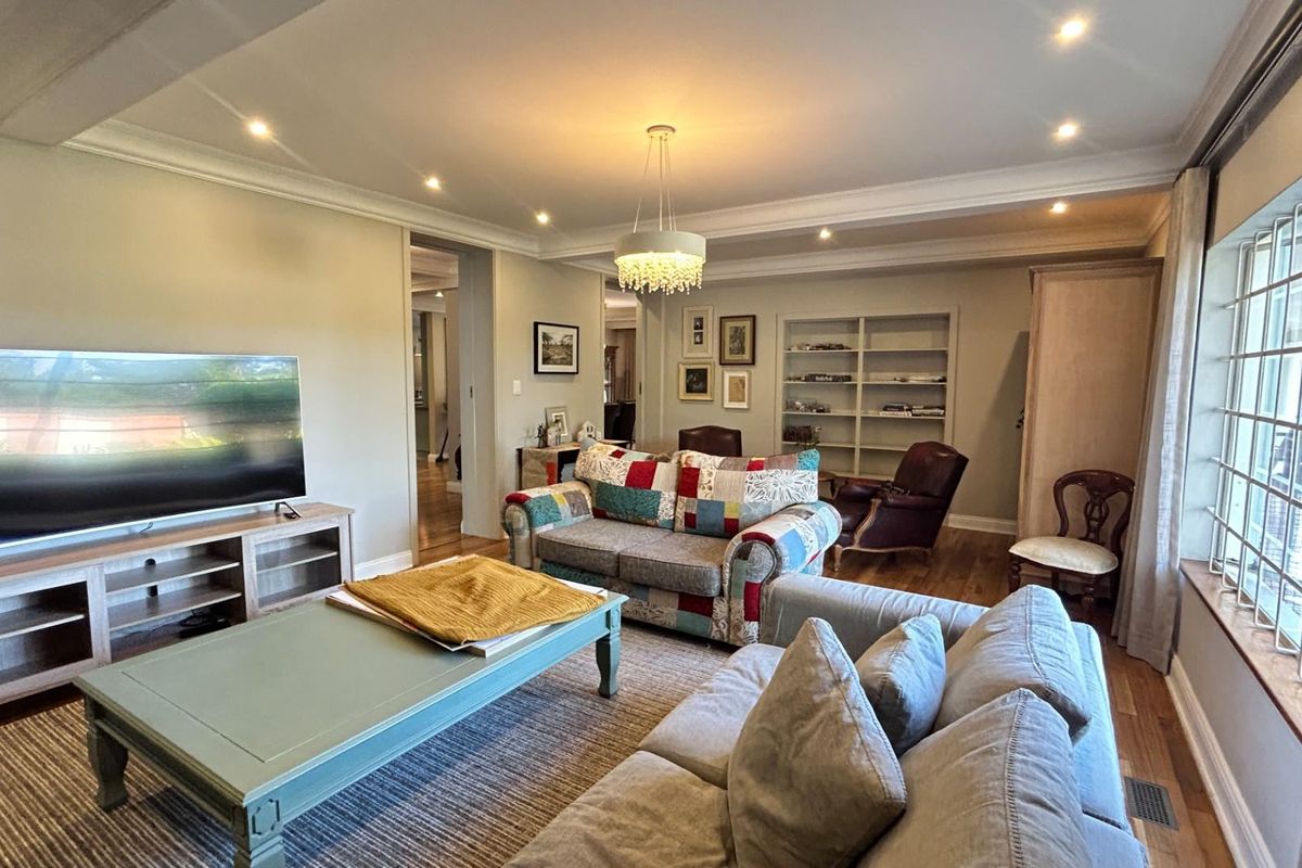 A spacious living room featuring recessed ceiling lighting, crown molding, hardwood flooring, and built-in shelving, creating a comfortable and well-defined living area.