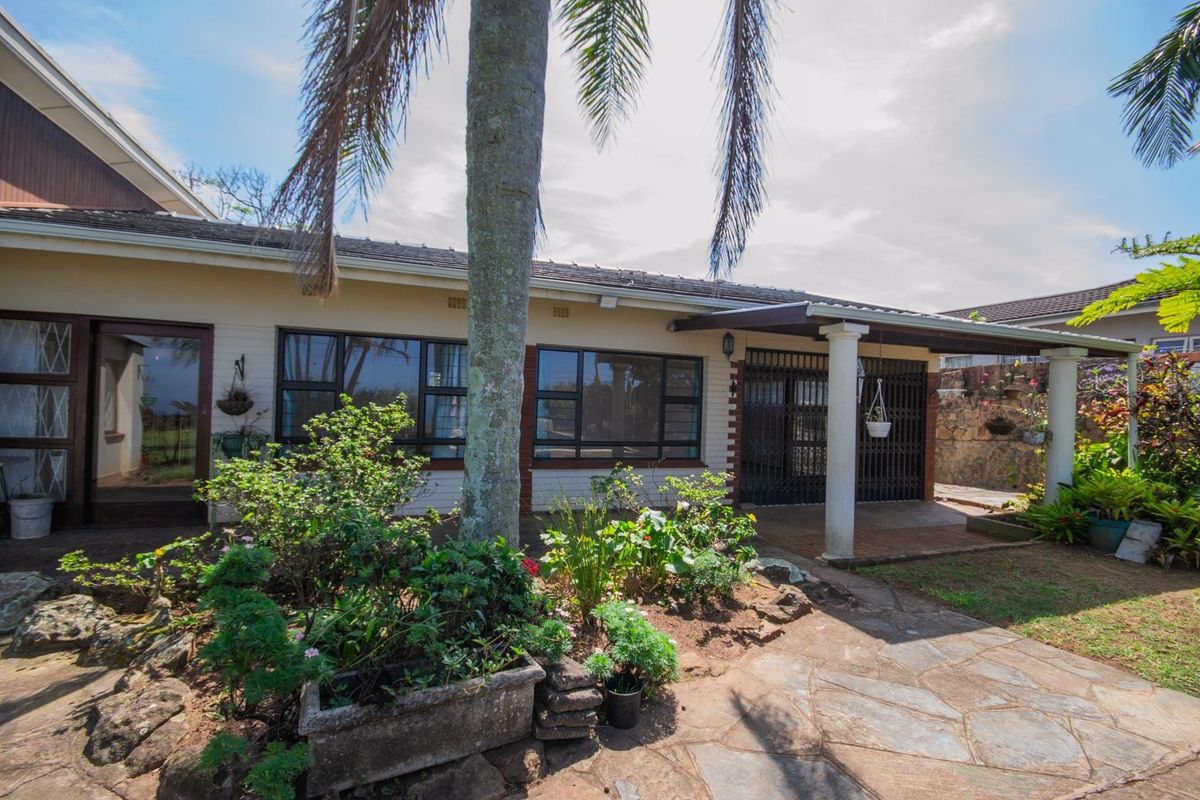 Rear exterior view of the house featuring a covered patio area, paved walkway, and established garden landscaping.