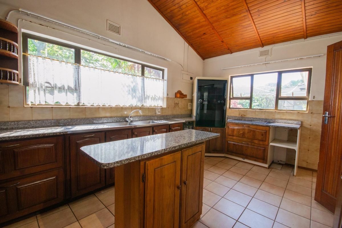 A functional kitchen featuring wooden cabinetry, granite-look countertops, tiled flooring, and a vaulted timber ceiling with ample natural light.