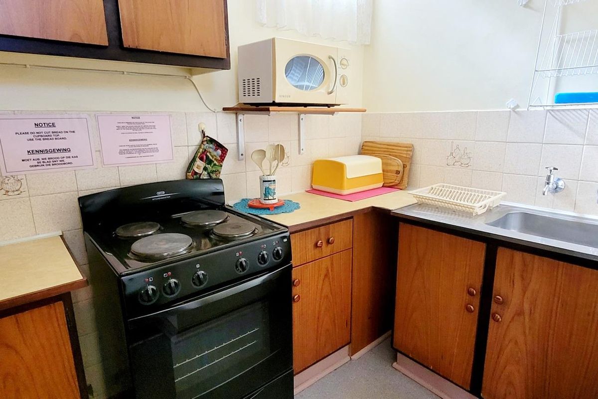 A compact kitchen featuring wooden cabinetry, a freestanding electric stove, and a single basin sink with tiled splashbacks.