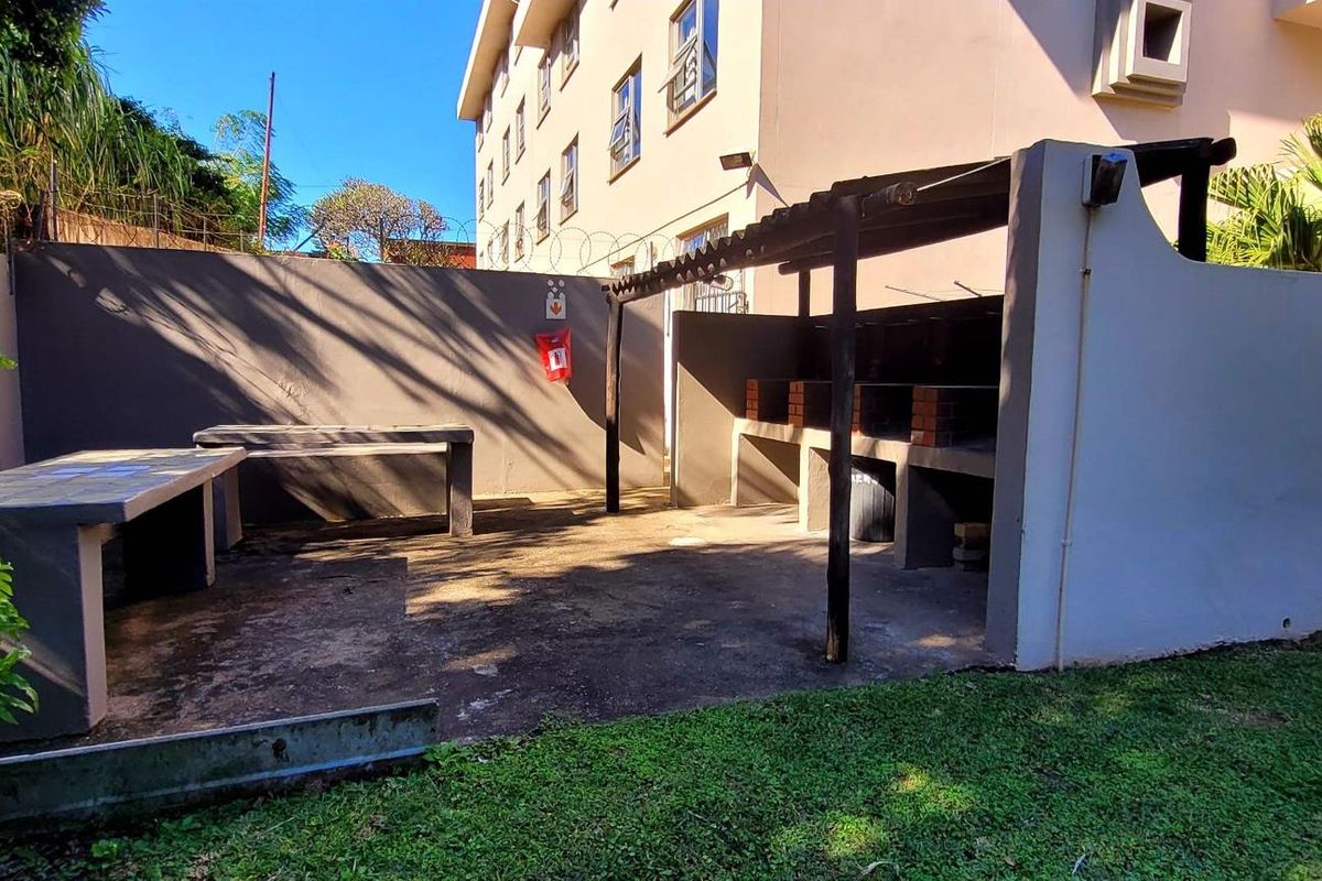 Outdoor entertainment area featuring a built-in brick braai, concrete prep surfaces, and a timber pergola set within a communal garden space.
