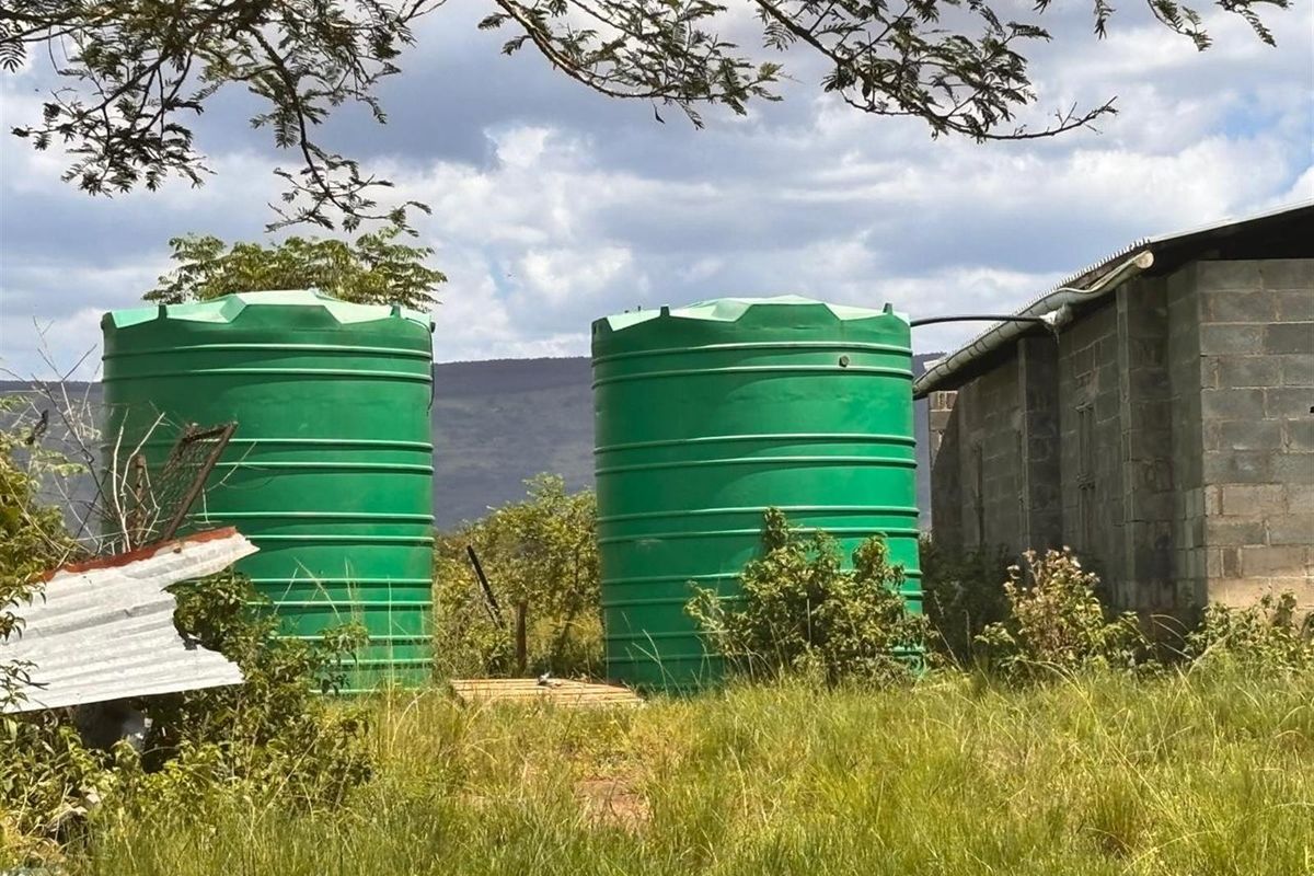 Exterior view of the farm property featuring two large green water storage tanks positioned next to a concrete block utility structure.