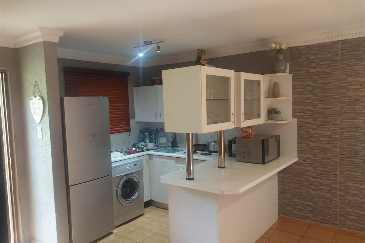 Compact kitchen featuring built-in cabinetry, a breakfast bar, tiled flooring, and a decorative stone-look feature wall.