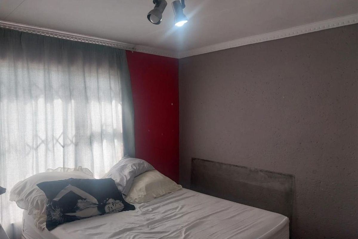 A bedroom featuring a textured accent wall, ceiling track lighting, and a window fitted with a security gate.