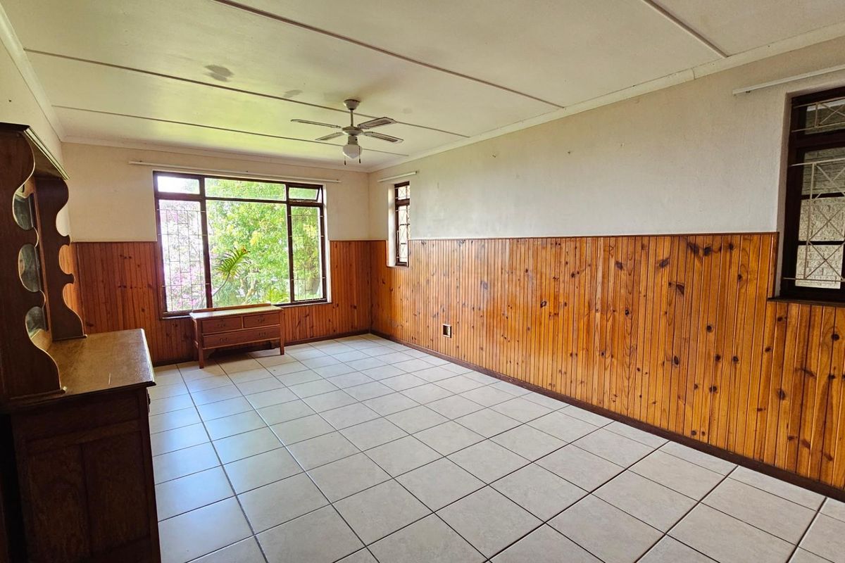 Spacious living area featuring tiled flooring, timber wall paneling, and a ceiling fan, offering a neutral canvas for potential updates.