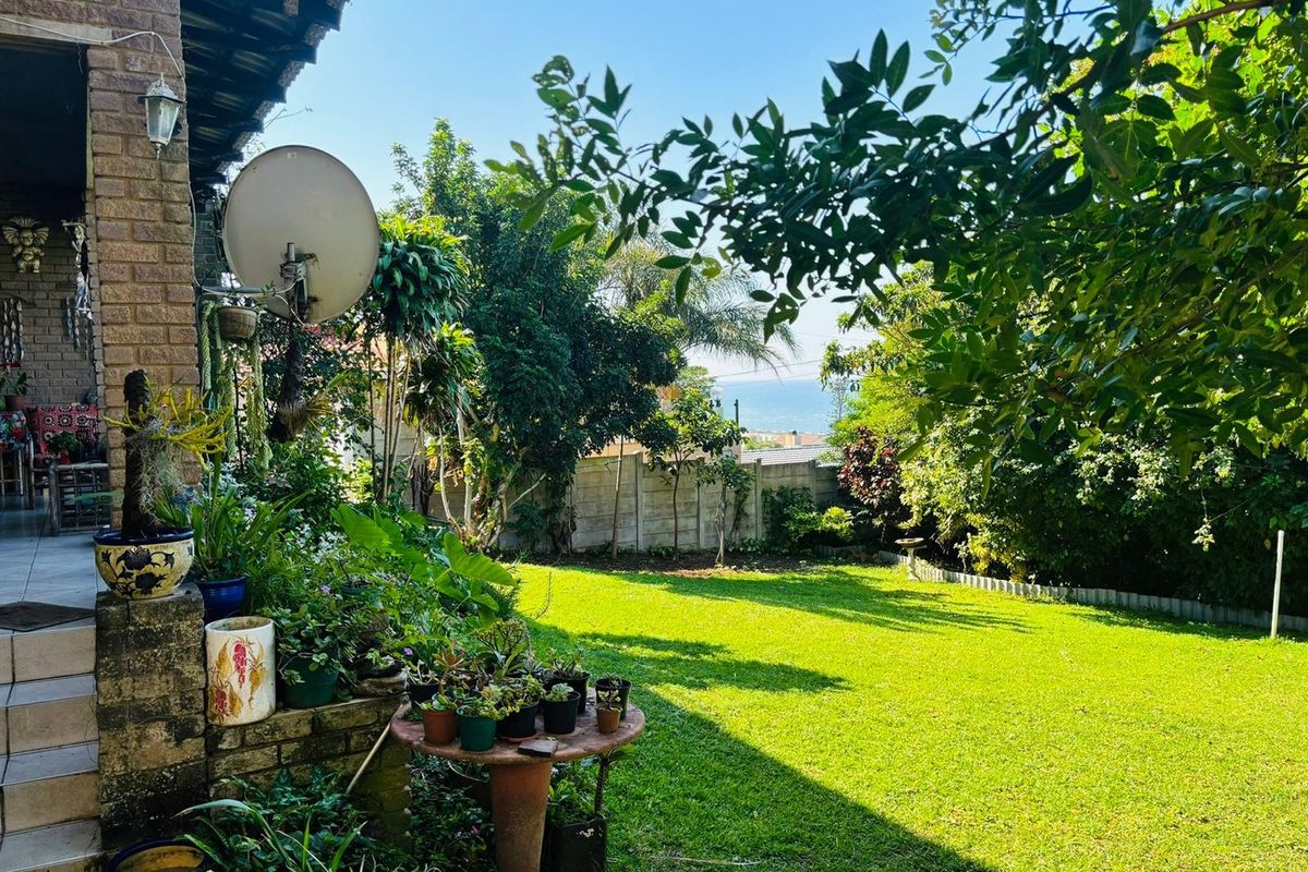 A view of the rear garden featuring a lawn, mature trees, and a partial view of the ocean in the distance.