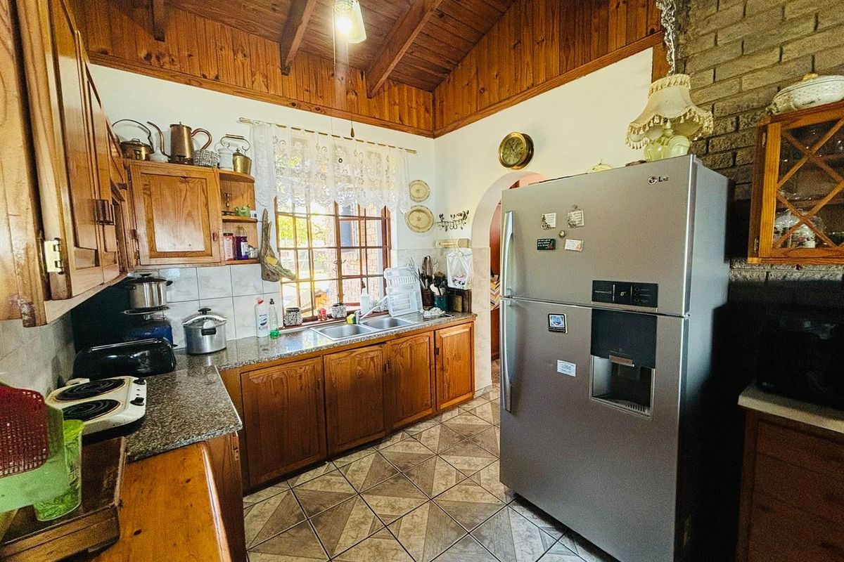 A rustic kitchen featuring timber cabinetry, exposed wooden ceiling beams, granite countertops, and a brick feature wall.