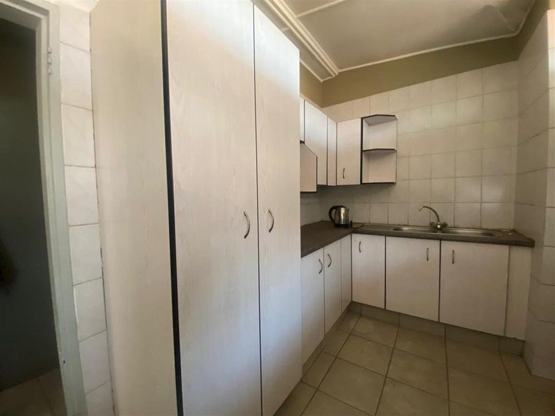 A functional kitchen featuring white cabinetry, tiled walls, a stainless steel sink, and tiled flooring.
