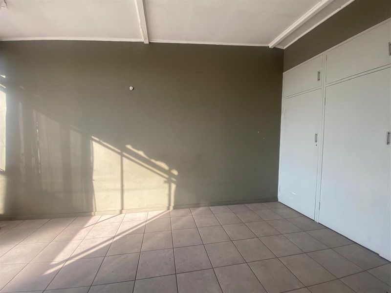 A vacant bedroom featuring neutral tiled flooring, built-in storage cupboards, and a simple ceiling finish.