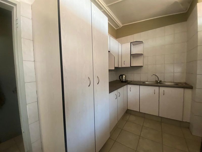 A functional kitchen featuring white cabinetry, tiled splashbacks, and a stainless steel sink, offering a clean and practical layout.