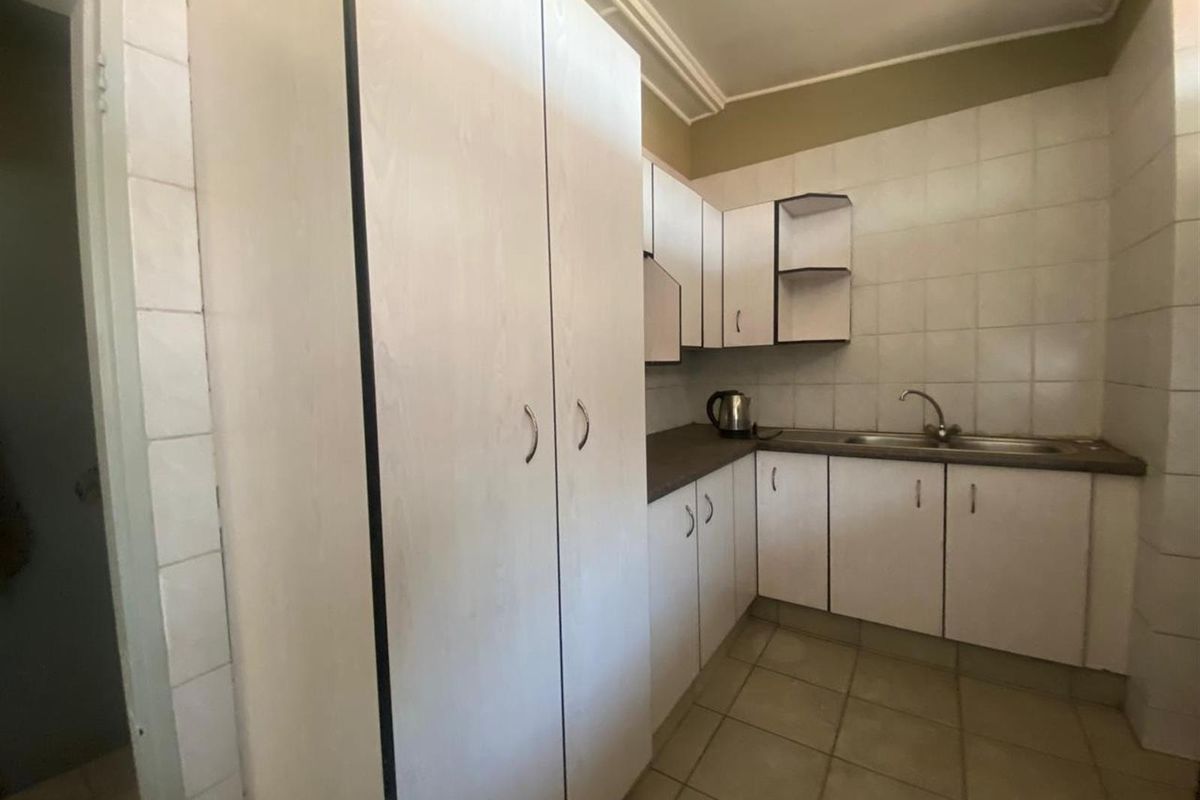A functional kitchen featuring white cabinetry, tiled splashbacks, and a stainless steel sink, offering a clean and practical layout.