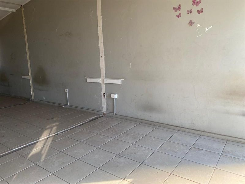 An empty, unfinished interior space featuring tiled flooring and exposed wall conduits, requiring significant cosmetic renovation and repair to restore to a habitable standard.
