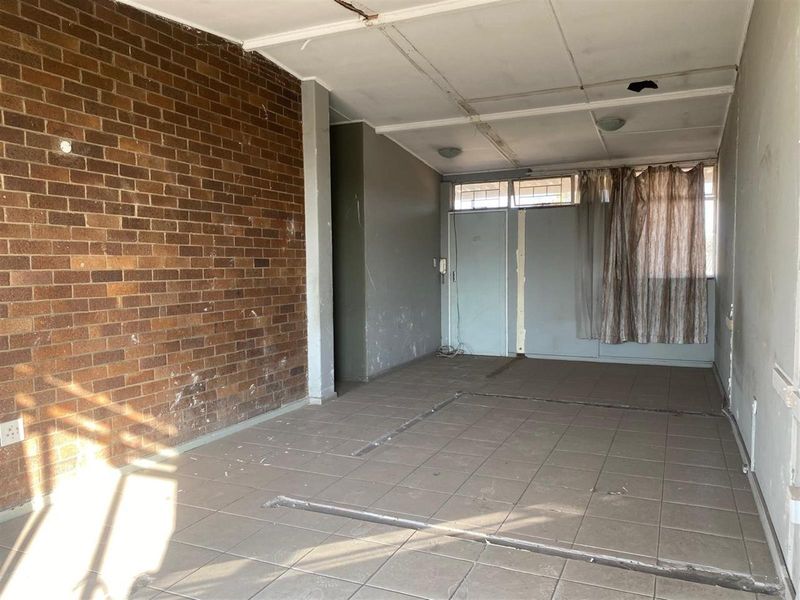 An empty living area featuring a prominent exposed brick feature wall, tiled flooring, and a drop ceiling in need of repair.