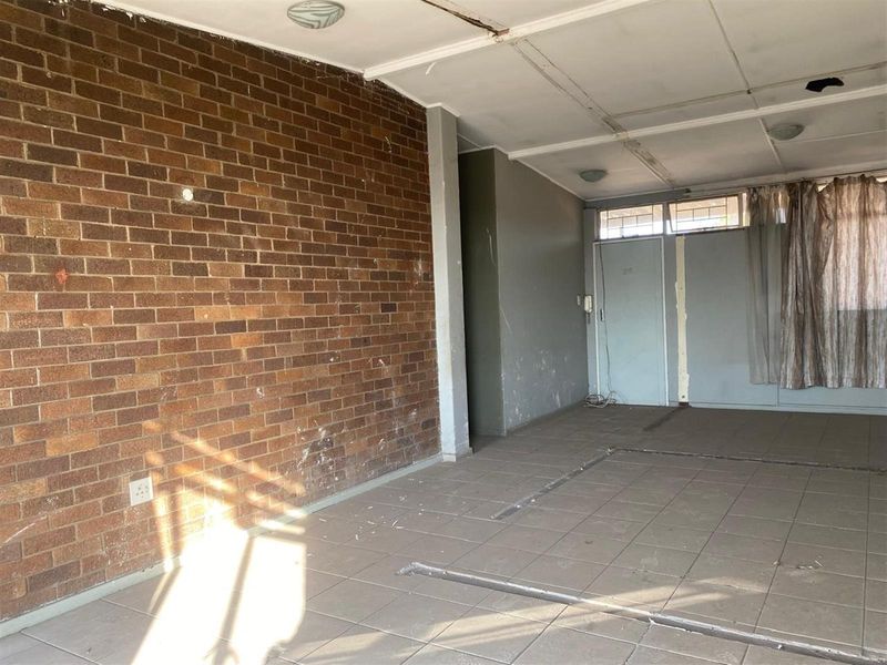 An empty living area featuring a prominent exposed brick feature wall, tiled flooring, and a drop ceiling in need of repair and refurbishment.