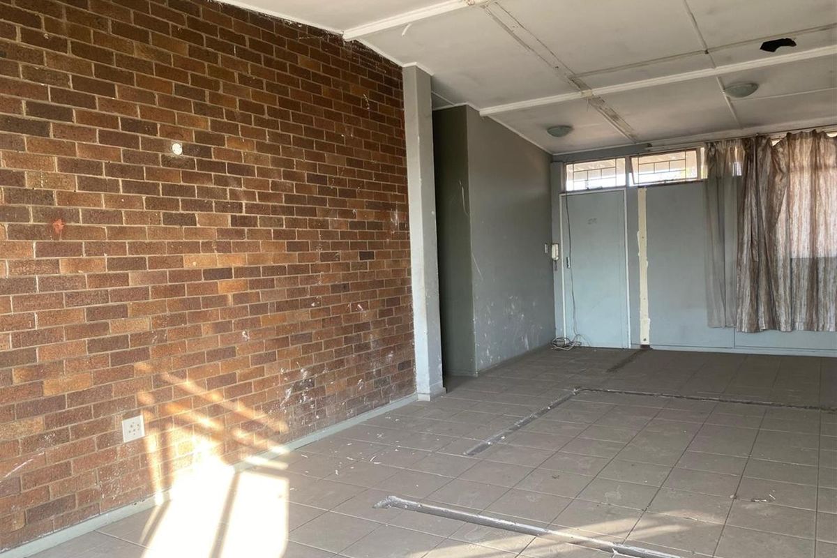 An empty living area featuring a prominent exposed brick feature wall, tiled flooring, and a drop ceiling in need of repair and refurbishment.