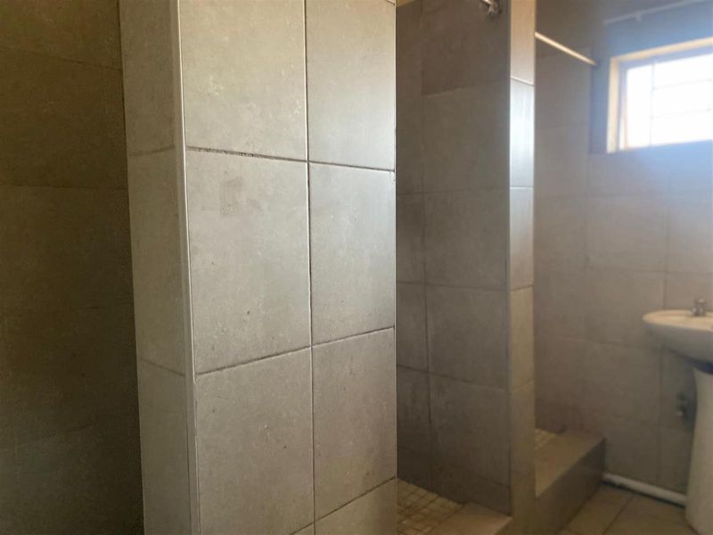 A functional bathroom featuring a tiled walk-in shower enclosure and a pedestal basin with neutral wall tiling.