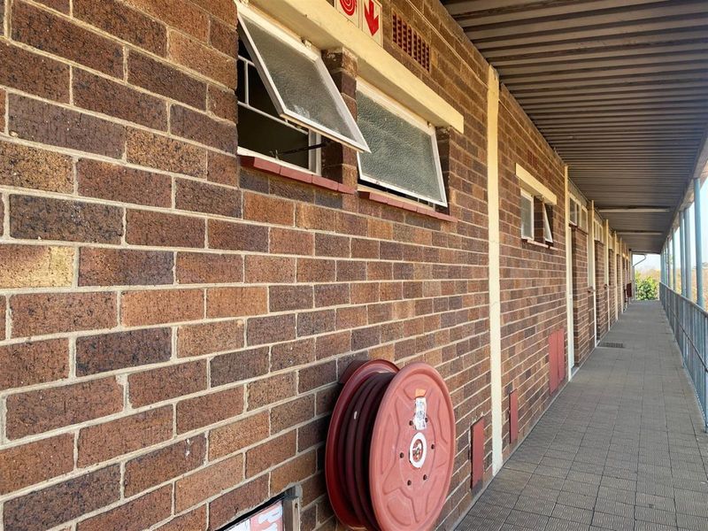 An exterior view of an apartment building walkway featuring exposed brick walls, top-hung windows, and a fire hose reel.
