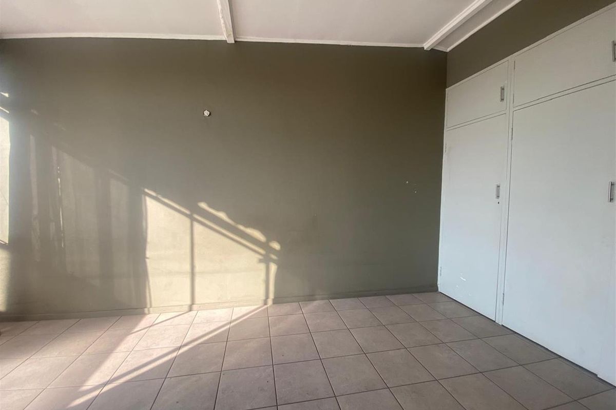 A vacant bedroom featuring neutral tiled flooring, built-in storage cupboards, and a simple ceiling finish.