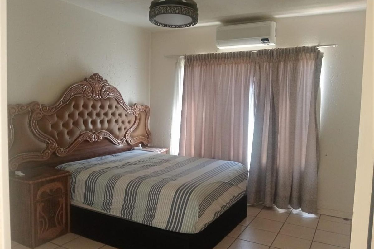 A bedroom featuring tiled flooring, a wall-mounted air conditioning unit, and a ceiling fan with integrated lighting.