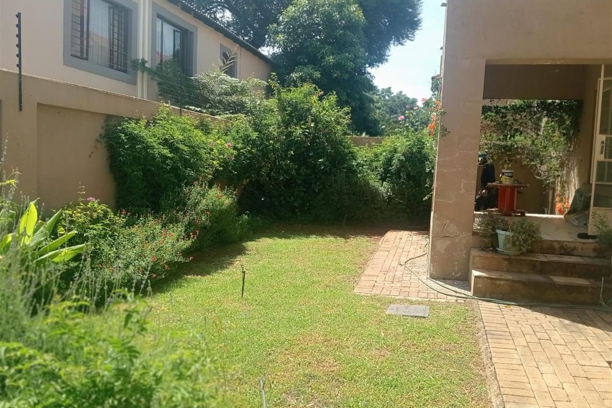 A private rear garden featuring a paved patio area, established greenery, and a lawn, providing a quiet outdoor space for the apartment.