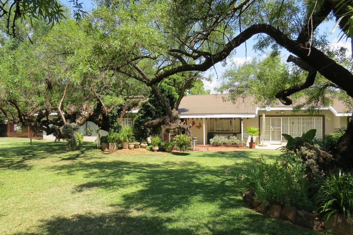 A spacious rear garden featuring a well-maintained lawn, mature trees, and a covered patio area attached to the main dwelling.