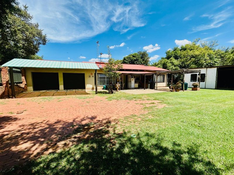 Rear view of the property featuring a double garage, paved driveway, and a covered patio area set within a spacious garden.