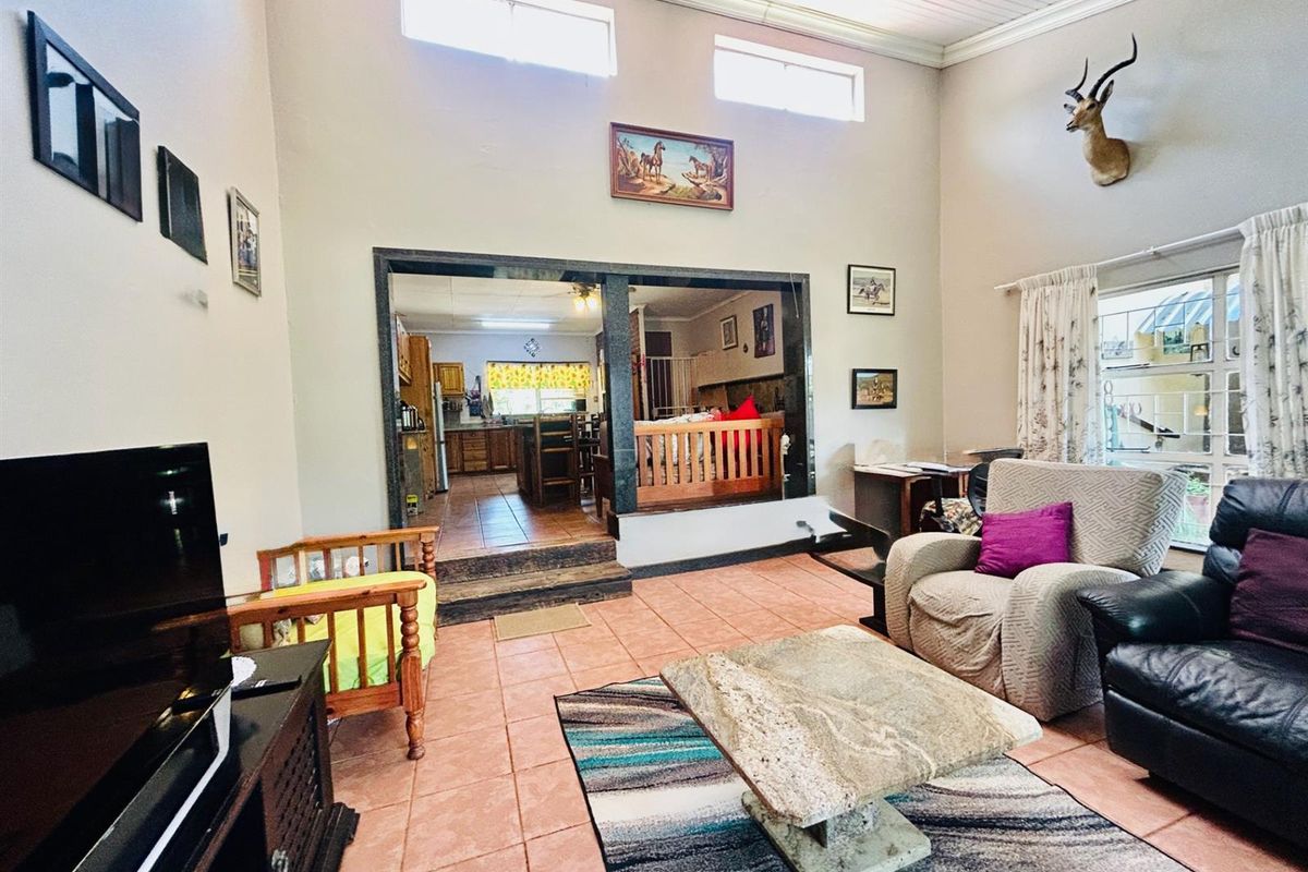 Spacious living room featuring high vaulted ceilings, clerestory windows, and a granite-trimmed doorway leading to the kitchen area with tiled flooring throughout.