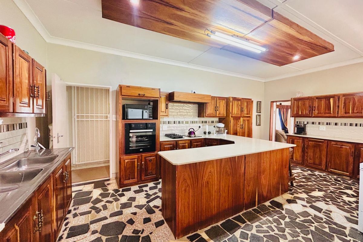 Spacious kitchen featuring extensive wooden cabinetry, a central island with stone countertops, built-in oven, and unique stone-patterned flooring.