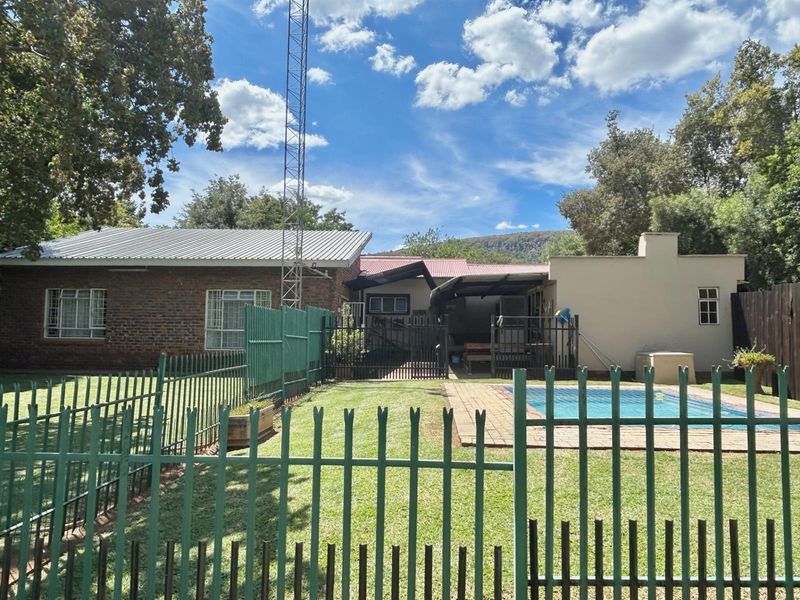 Rear view of the property featuring a swimming pool, paved surround, and a fenced garden area with a mix of brick and plastered wall finishes.