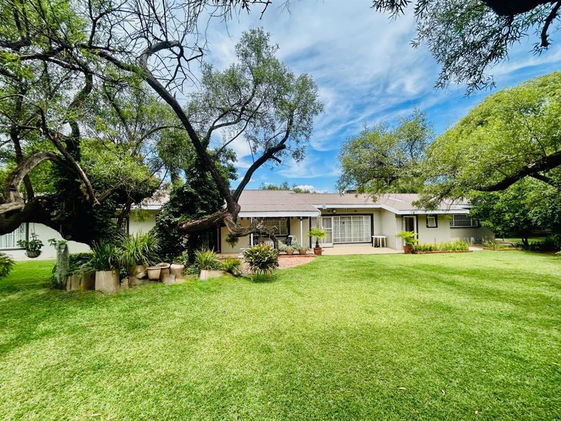 Spacious rear garden featuring a paved patio area, mature trees, and a well-maintained lawn leading to the main dwelling.