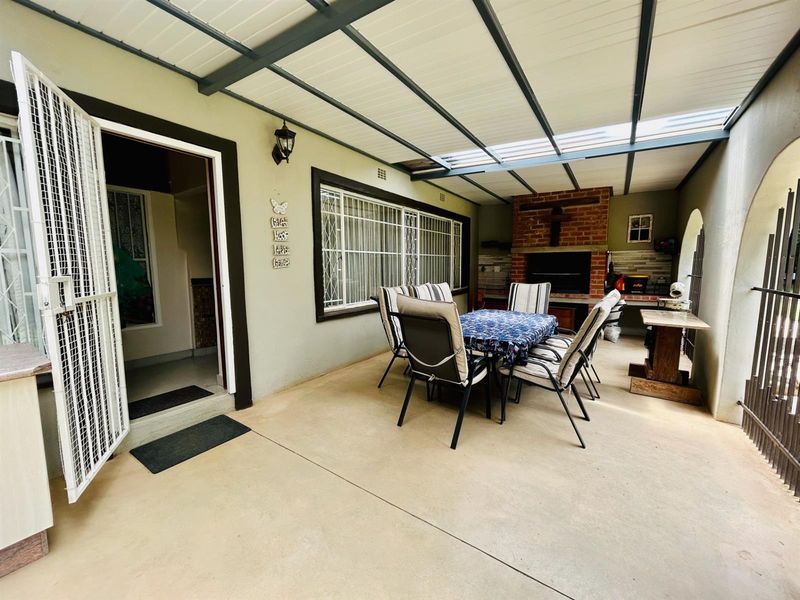 A covered outdoor patio area featuring a built-in brick braai, concrete flooring, and direct access to the interior through a security gate.