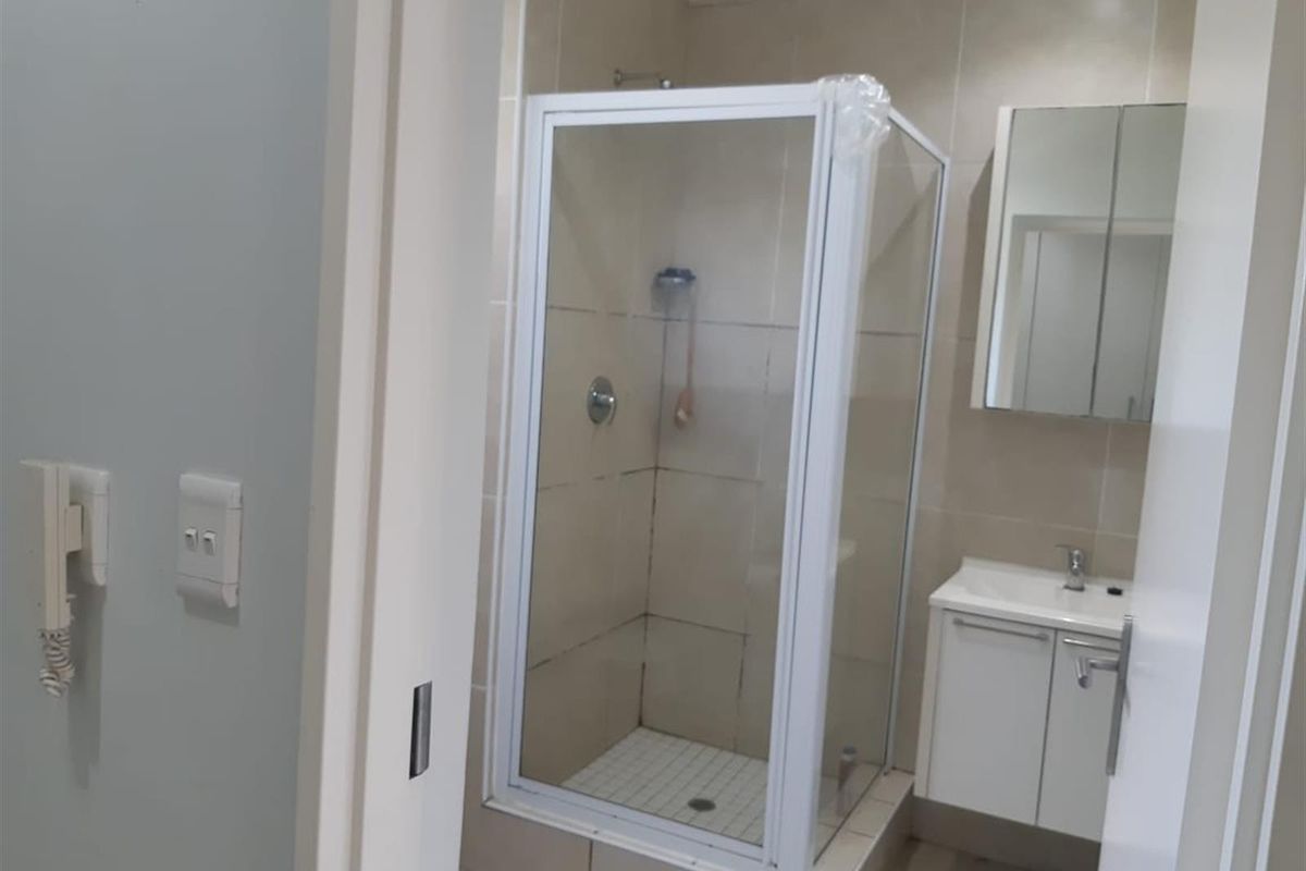 A compact bathroom featuring a glass-enclosed shower, a wall-mounted vanity with a basin, and a mirrored medicine cabinet.