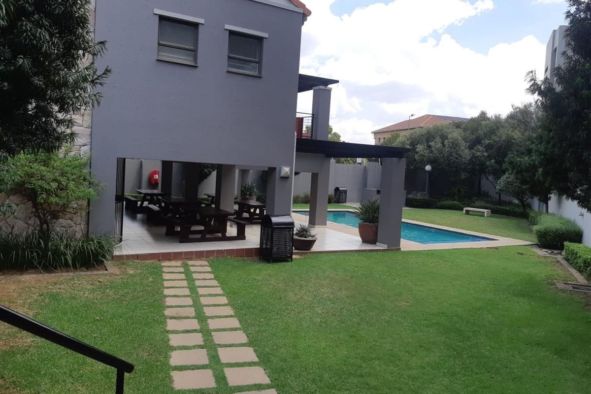 A rear view of the apartment building featuring a covered patio area, a swimming pool, and a well-maintained garden.