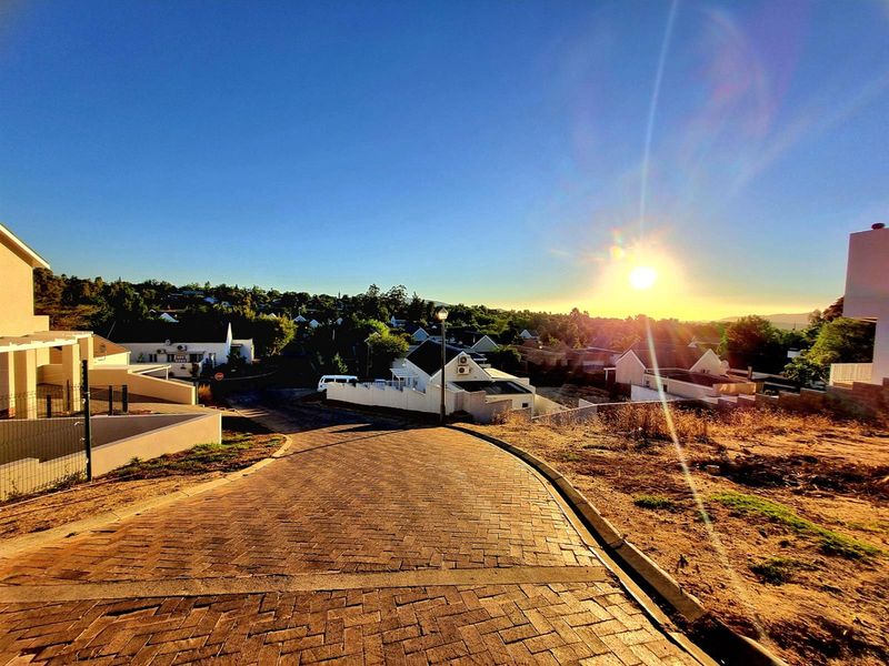 A scenic street view looking down a paved residential driveway towards the surrounding neighborhood at sunset.