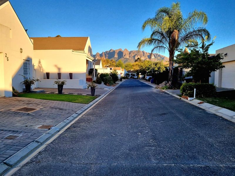 A clear street view of a residential neighborhood featuring paved roads, well-maintained driveways, and scenic mountain views in the background.