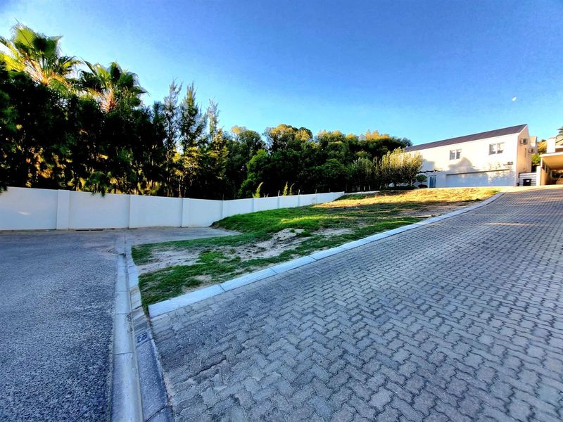 A view of the front of the residential vacant land plot, featuring a paved driveway, perimeter walling, and established landscaping.