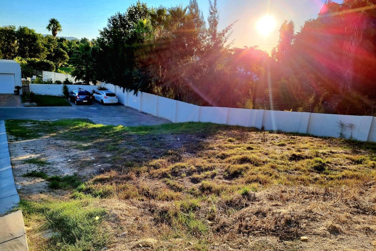 A vacant residential plot featuring a paved driveway, perimeter walling, and established trees, offering a clear space ready for development.