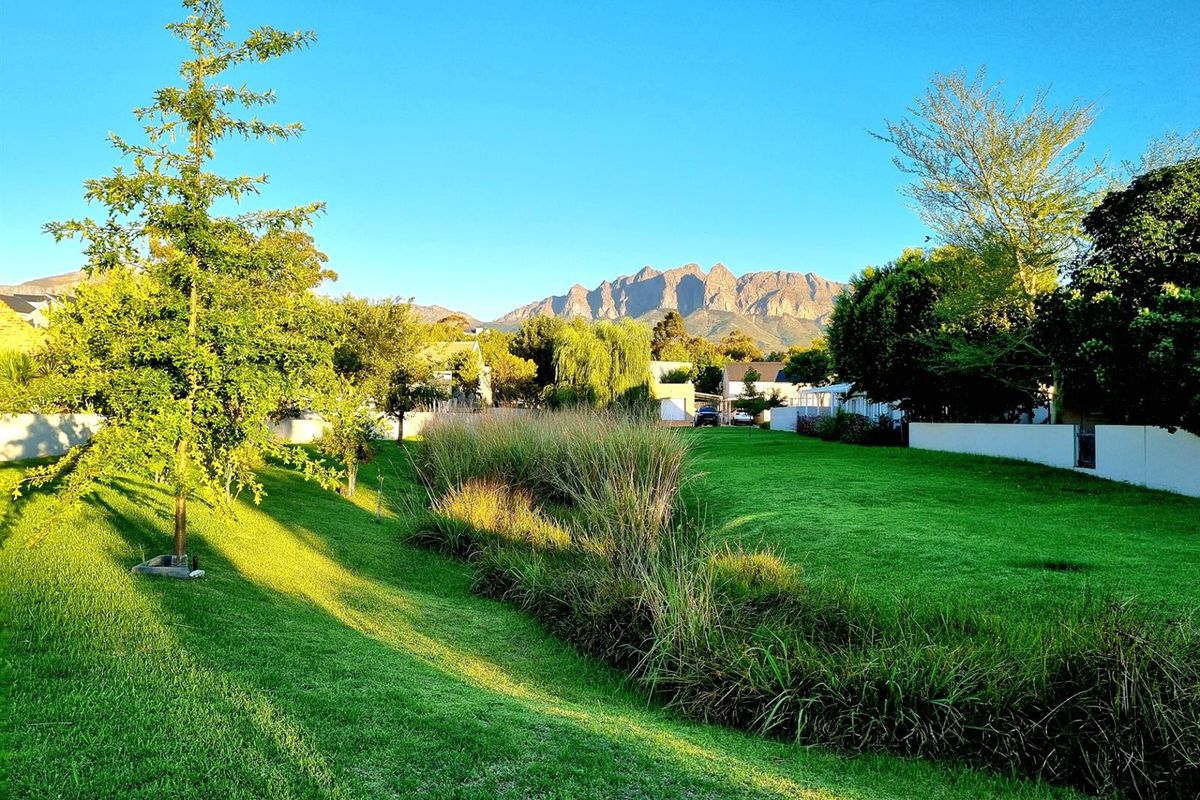 A scenic view of a well-maintained residential lawn and garden area with a prominent mountain range in the background.