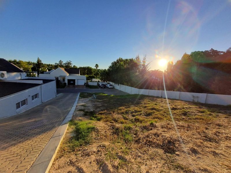 A vacant residential plot featuring a paved driveway and boundary wall, situated in a developed neighborhood with sunset views.