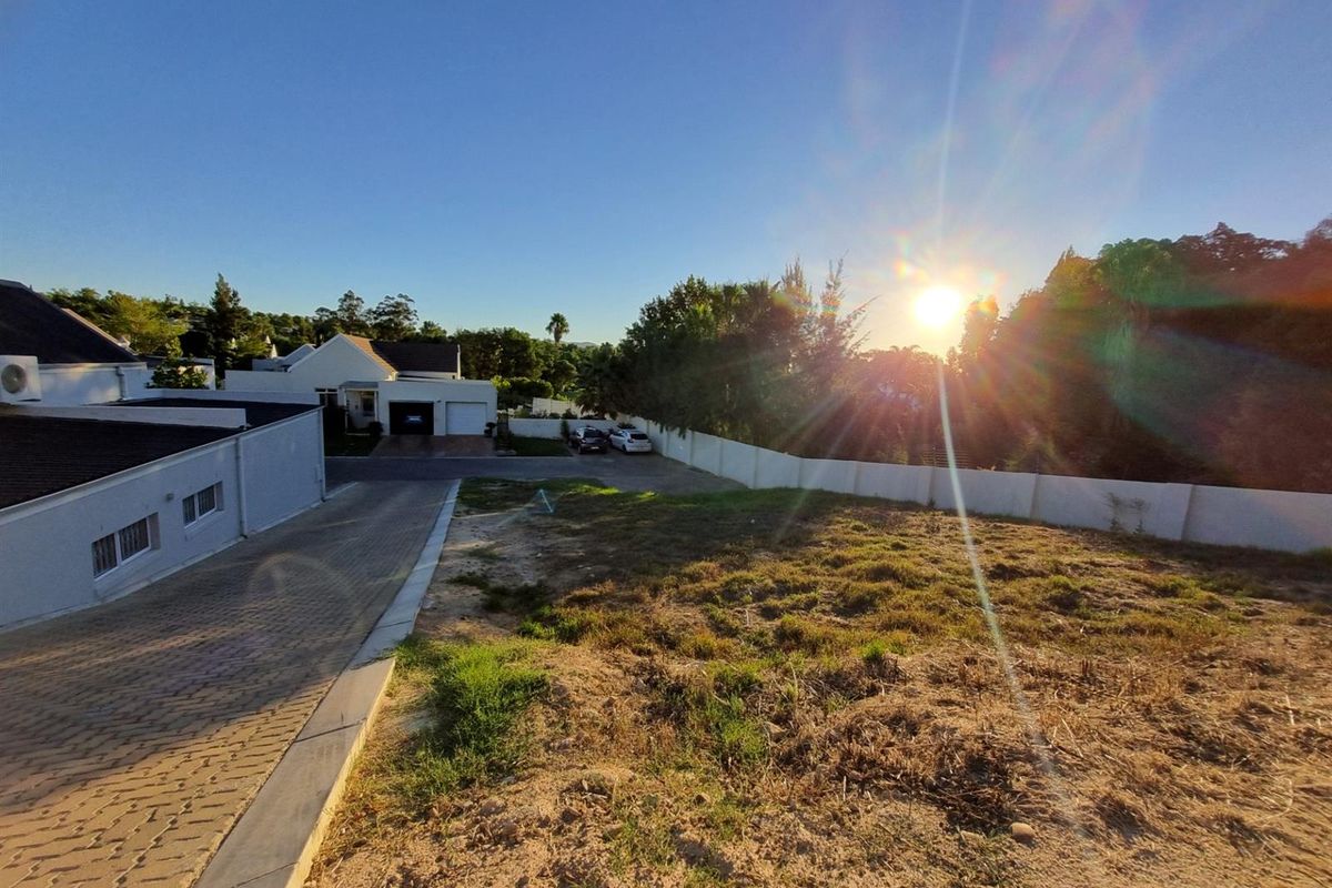 A vacant residential plot featuring a paved driveway and boundary wall, situated in a developed neighborhood with sunset views.