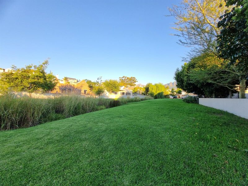 A well-maintained, expansive green lawn bordered by mature trees and a boundary wall, offering a peaceful outdoor setting.
