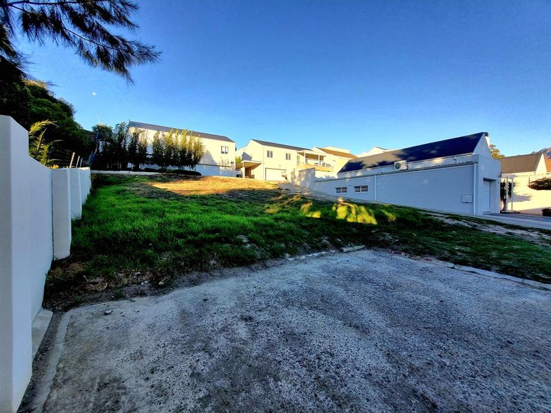 A vacant residential plot featuring a concrete driveway, boundary wall, and a gentle upward slope, situated in a developed neighborhood.