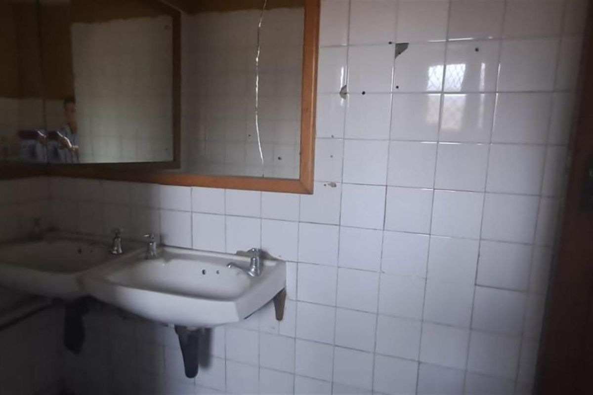 A dated bathroom featuring dual wall-mounted sinks, tiled walls, and a large mirror, currently in need of significant renovation and repair.