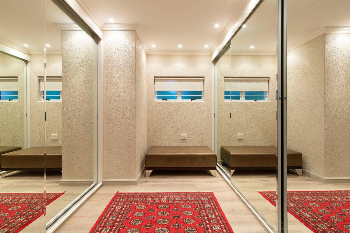 A well-lit dressing room or walk-in closet featuring floor-to-ceiling mirrored sliding wardrobe doors, recessed downlighting, and light-toned laminate flooring.